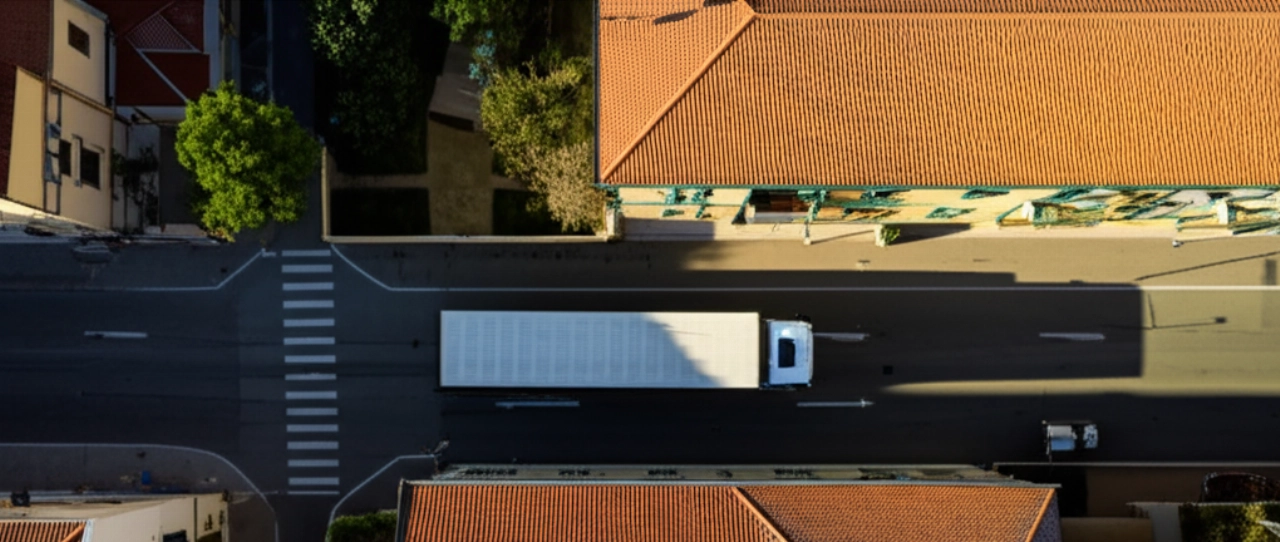 Vista aerea iperrealistica di un camion dei traslochi parcheggiato in una strada residenziale di Nuoro, che mostra l'architettura locale e la precisione logistica.